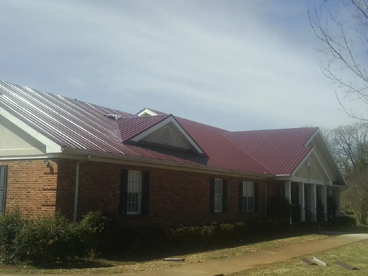 Red metal roof with gabled entries on a long brick building, from a Hail Damage Roof Repair job in Millwood