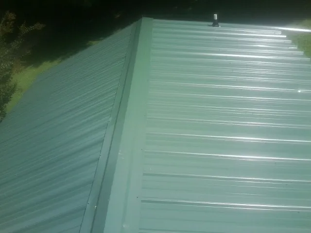 New green metal panels meeting at the ridge of a roof — Flat Roof Repair work by our crew in Millwood
