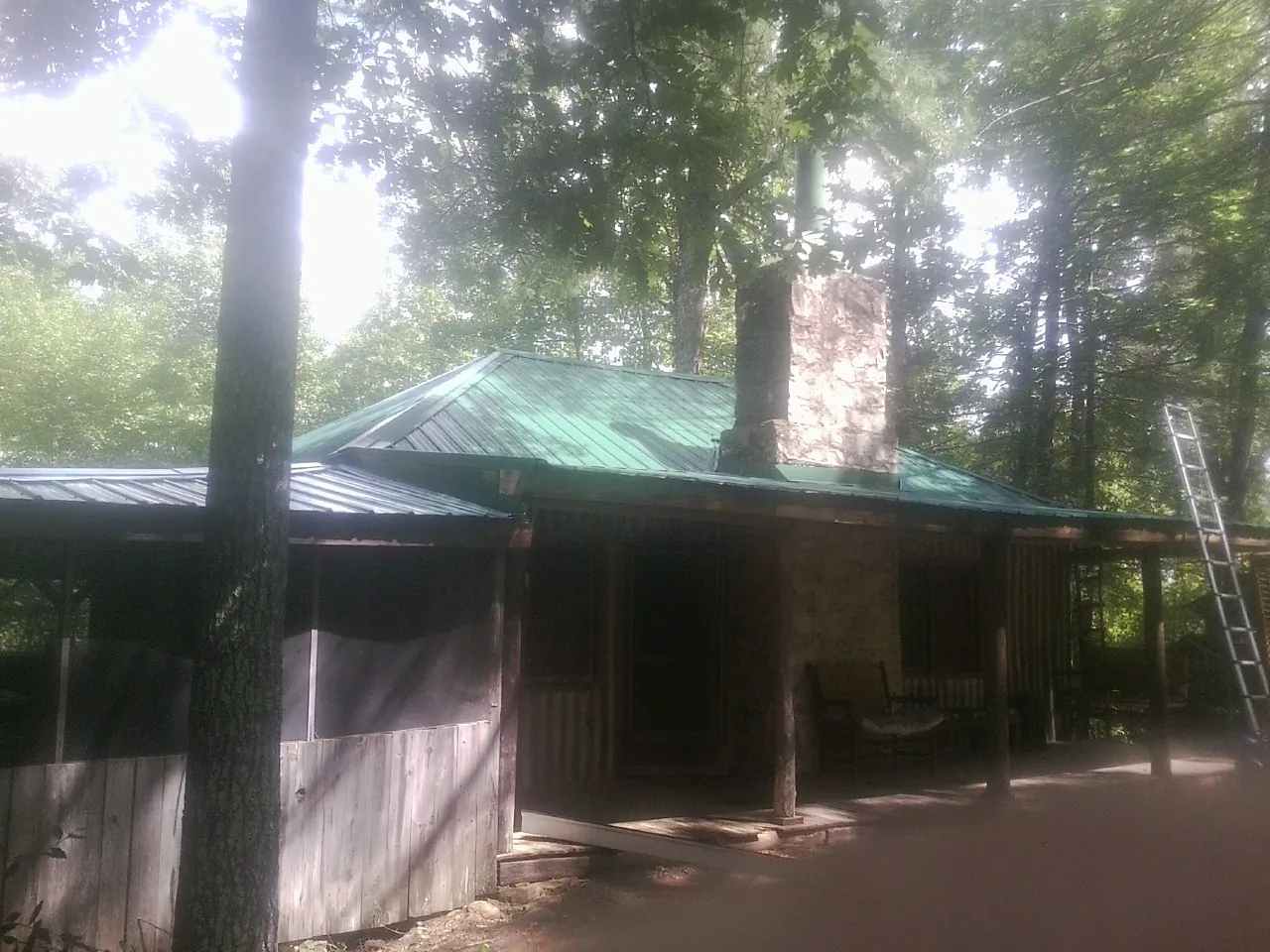 Green metal roof and stone chimney above a log cabin porch in Millwood